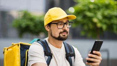 Caucasian man courier of food delivery with big thermal backpack on his back talking on smartphone